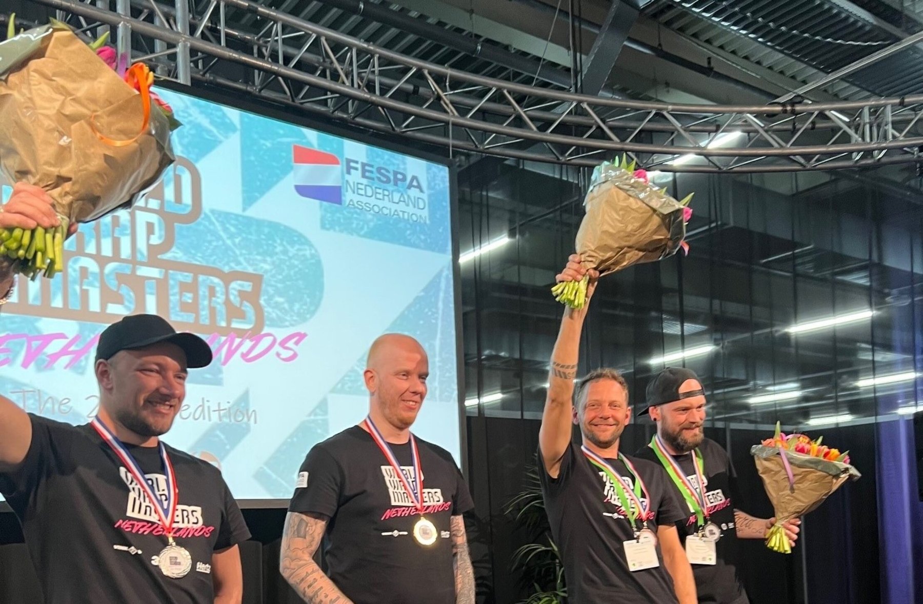 Four smiling winners of the Wrap Masters Netherlands competition holding medals and flowers on stage.