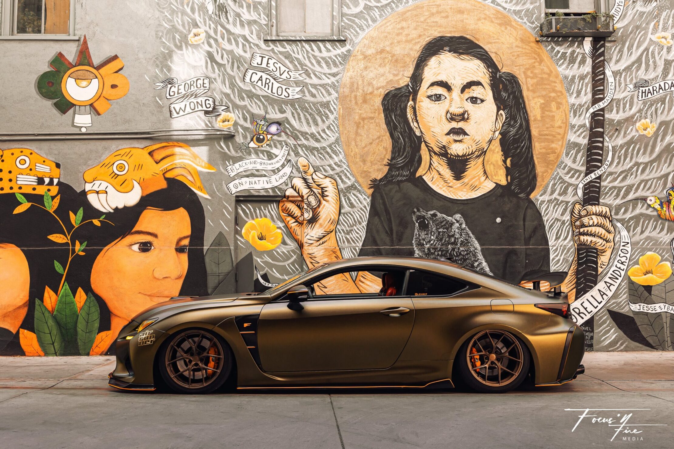 Custom wrapped bronze sports car parked against a vibrant street mural.