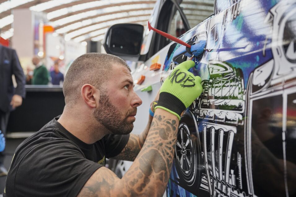 Vehicle wrapping competitor applies a graphic vinyl wrap to a car door using a squeegee tool.