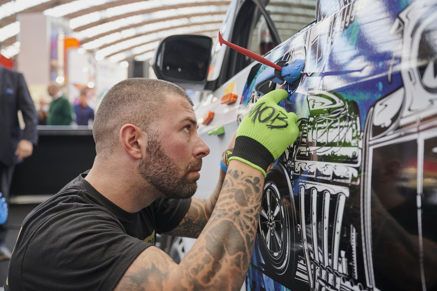 Vehicle wrapping competitor applies a graphic vinyl wrap to a car door using a squeegee tool.