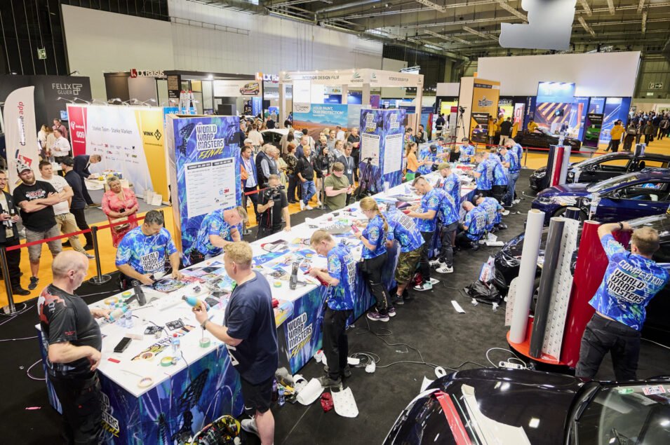 Vehicle wrapping competitors in matching blue shirts work on tasks at the FESPA World Wrap Masters Final event.