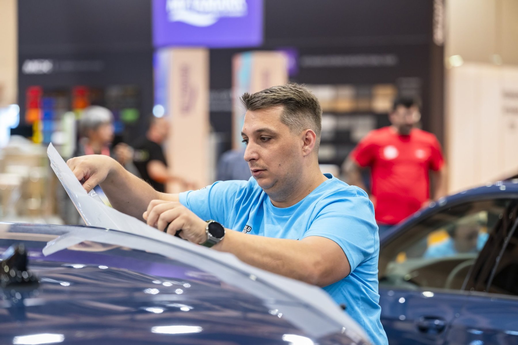 Vehicle wrapping competitor applying vinyl to a blue car bonnet.