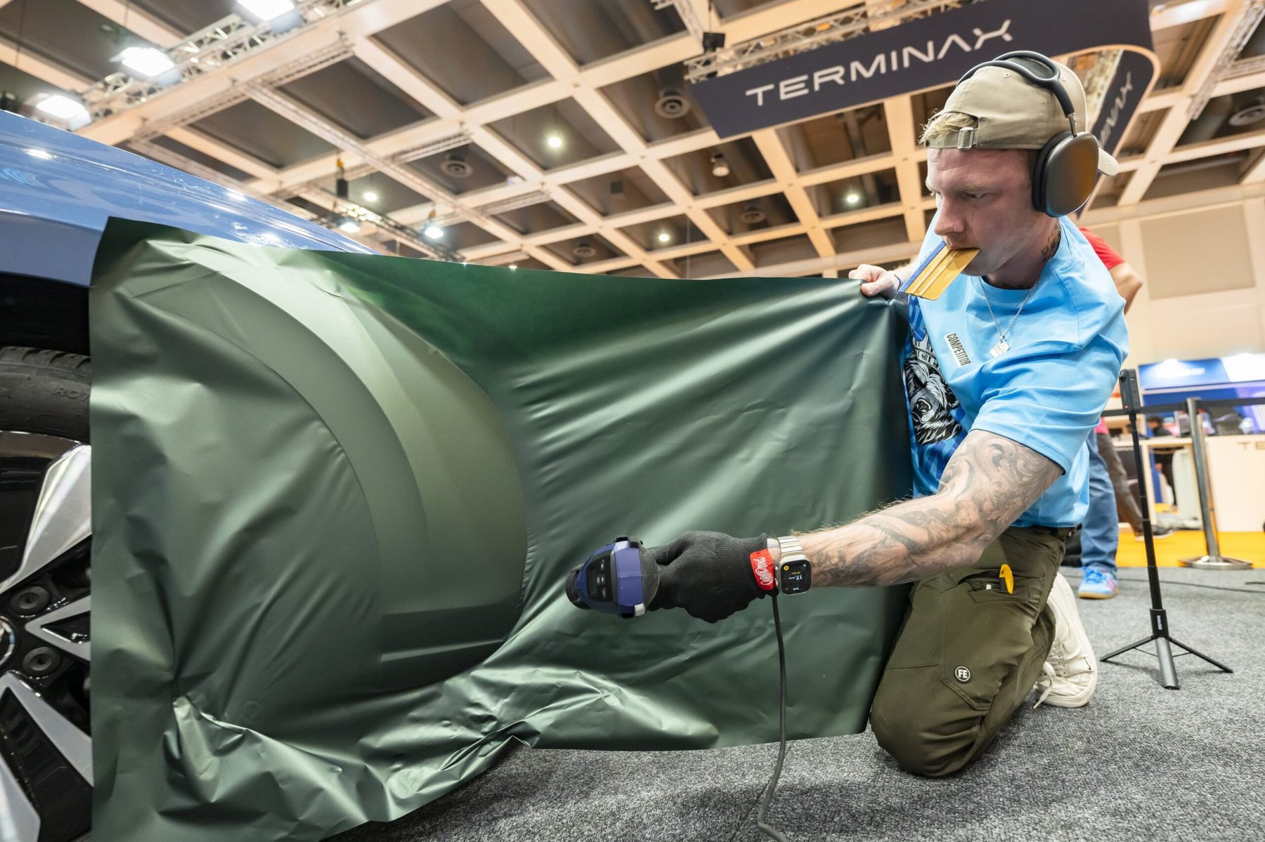 Wrap Masters competitor applying dark green vinyl wrap to a vehicle panel using a heat gun.