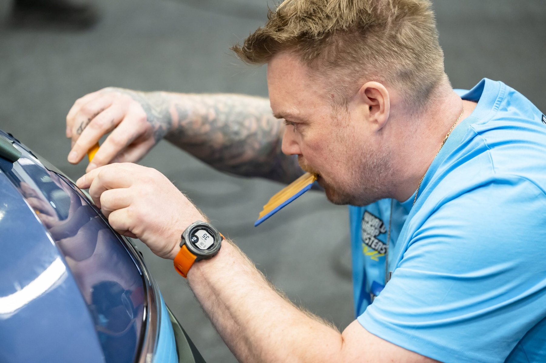Wrap Masters competitor applying vinyl wrap, holding a squeegee tool in his mouth.
