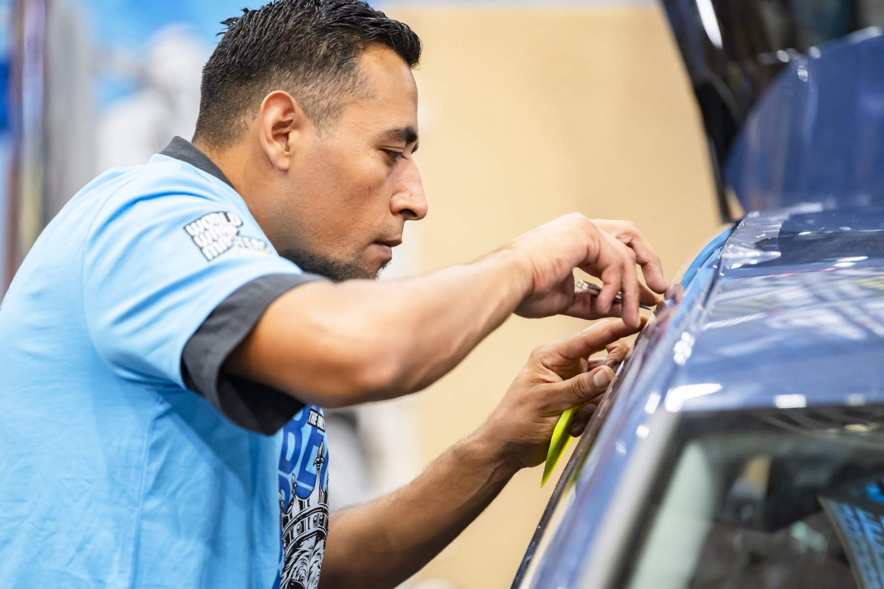 A competitor applies vinyl wrap to a blue vehicle during the FESPA Wrap Masters competition.