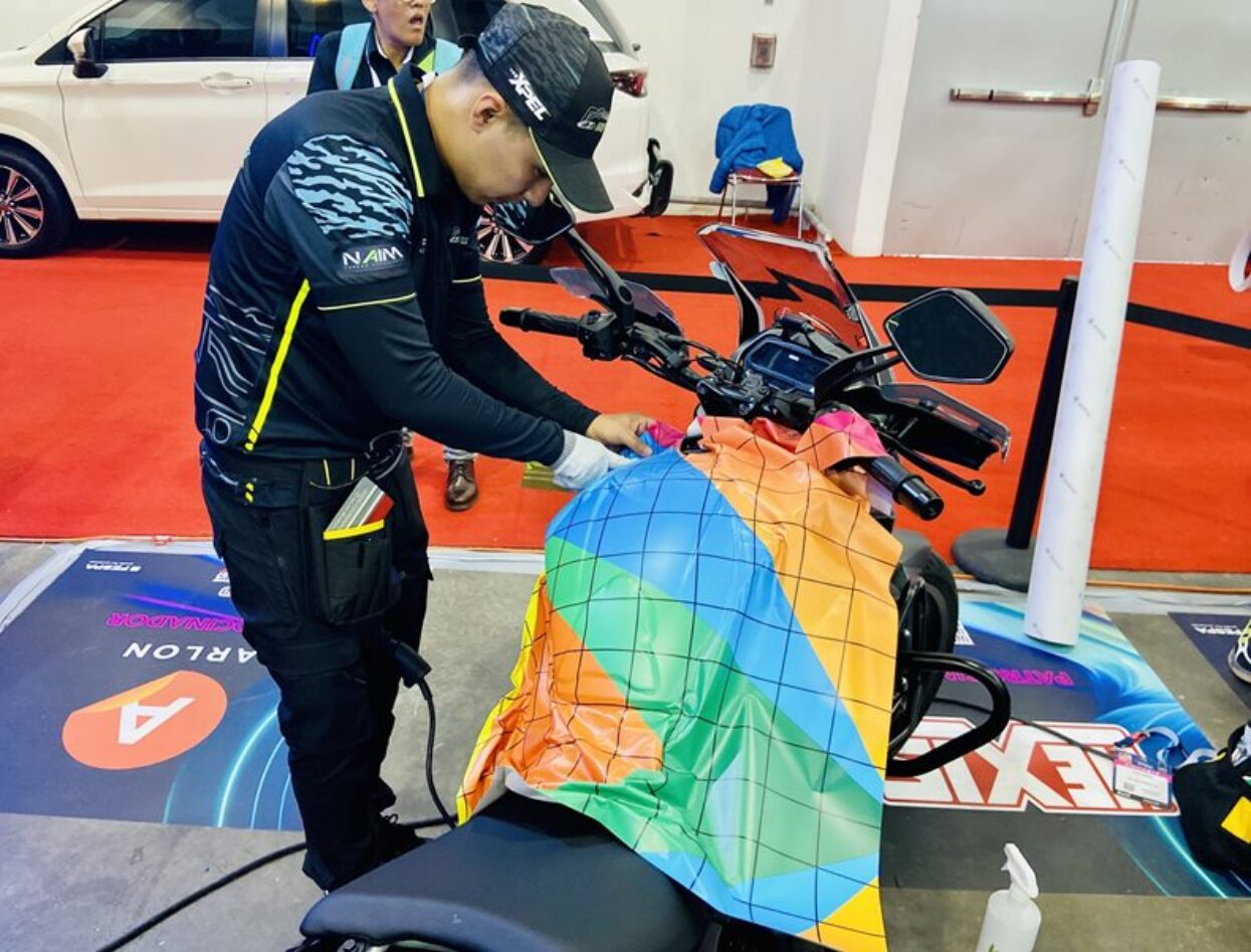 Wrapper applies a bright, geometric vinyl wrap to a motorcycle at a competition event.