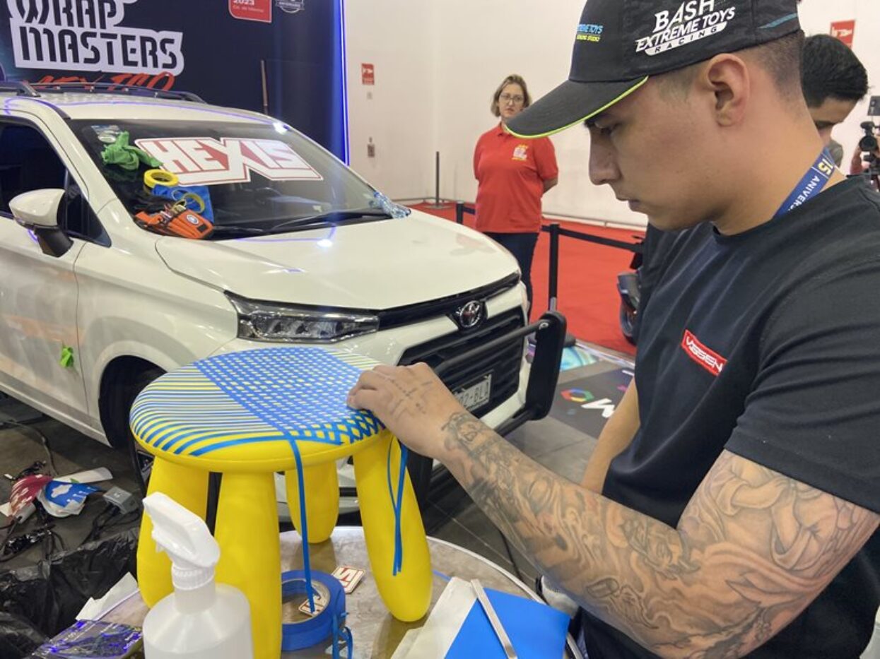 Close-up of a competitor wrapping a yellow stool with blue and yellow vinyl at the Wrap Masters event.