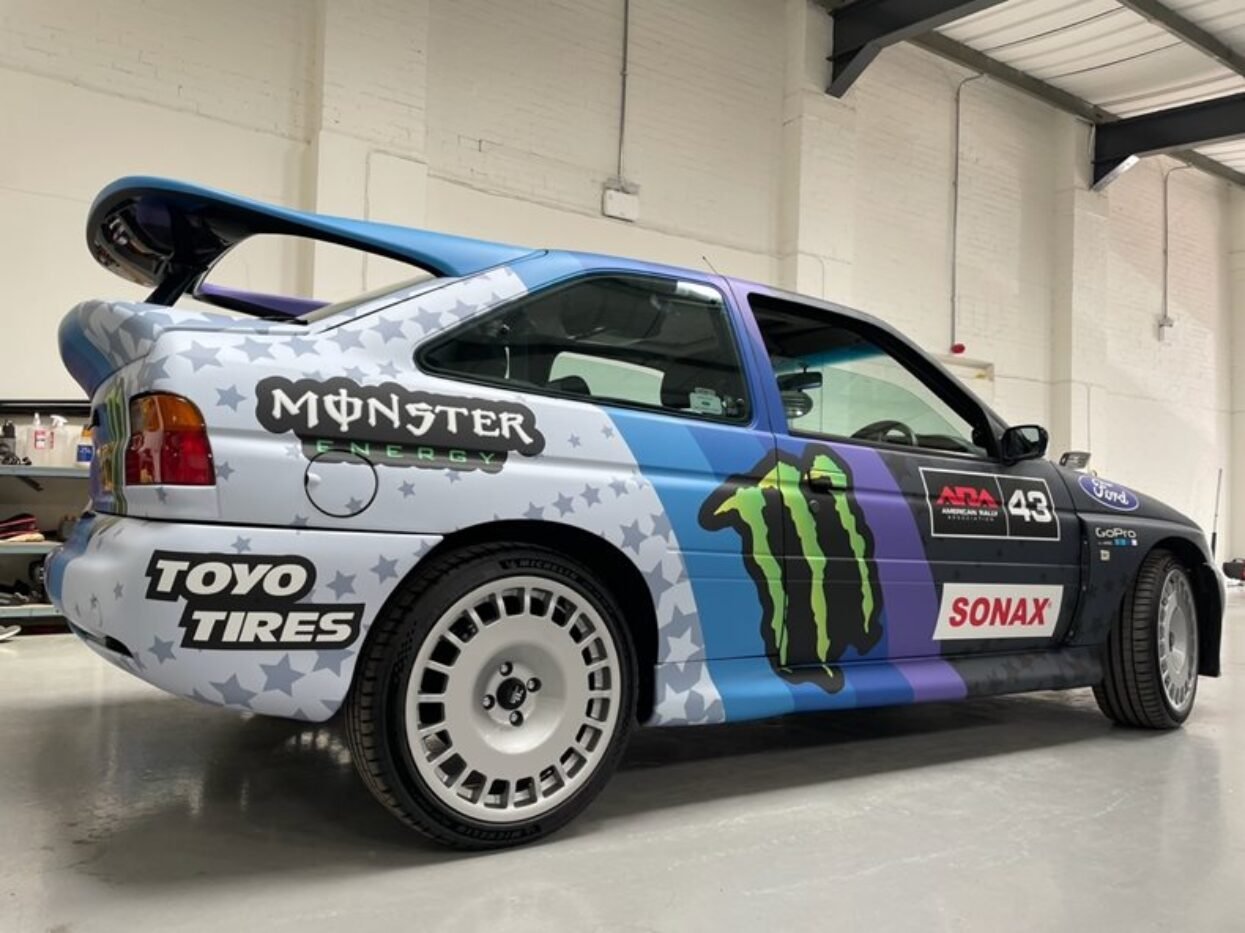 Competition rally car, wrapped in blue, purple, and grey vinyl, featuring Monster Energy and Toyo Tires branding.