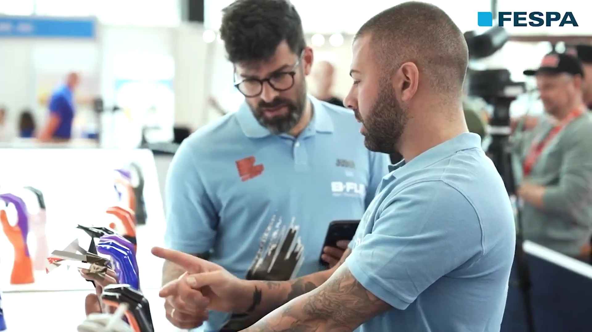 Attendees discussing the colourful Wrap Masters trophies at the FESPA exhibition.