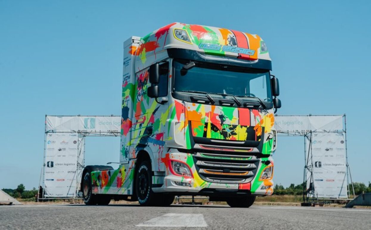 A DAF lorry cab wrapped in neon paint splatter vinyl, positioned near event arches.