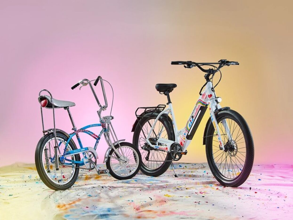A vintage blue chopper bike next to a modern white e-bike, both covered in colourful wraps, on a paint-splattered floor.```