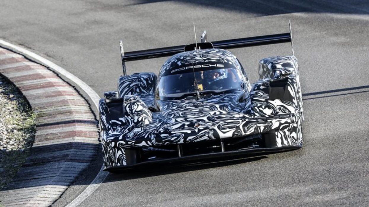 Porsche prototype race car with black and white camouflage wrap driving on a circuit.