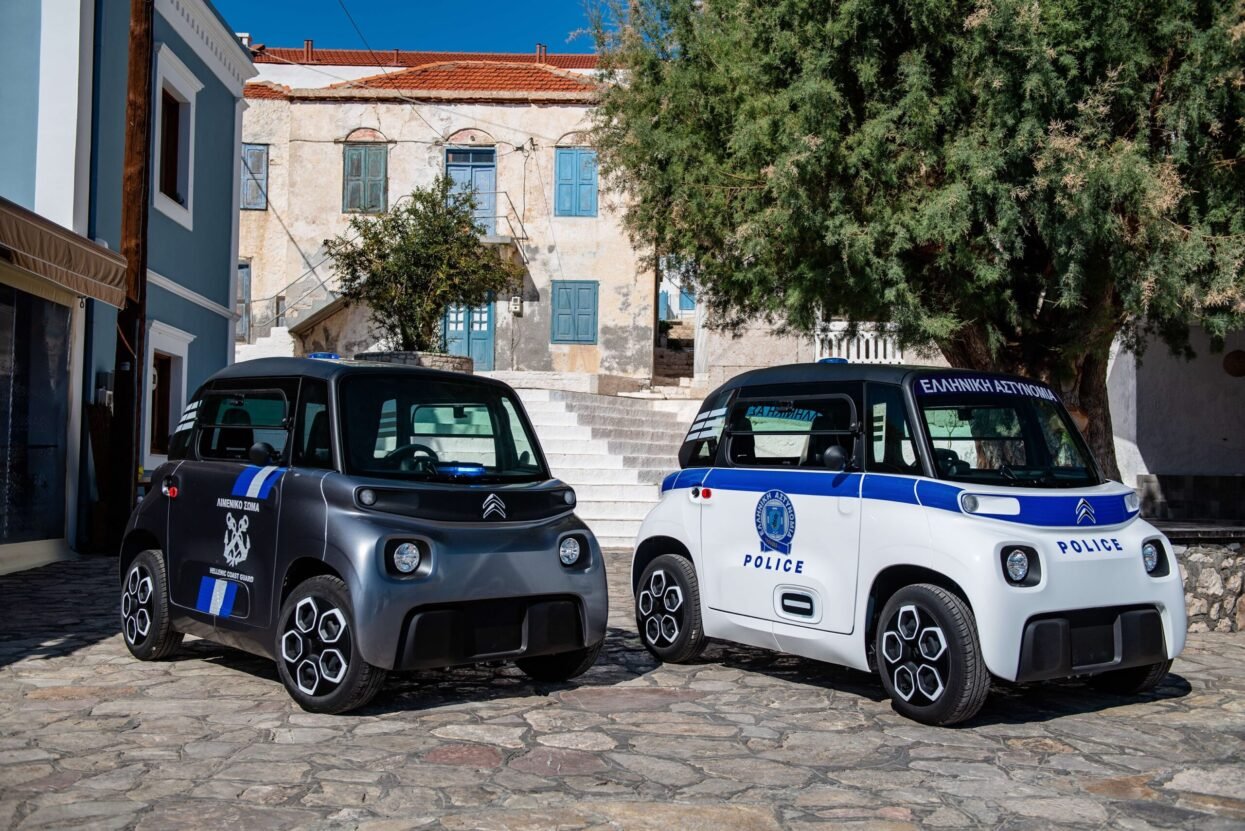 Grey Coast Guard and white Police wrapped Citroen Ami electric cars parked on a cobbled street.