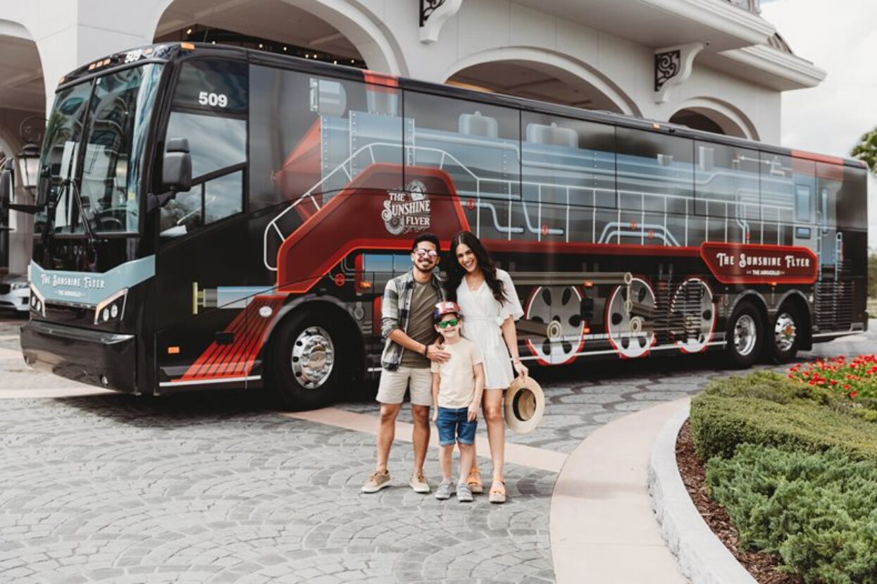 Family posing in front of a black coach featuring a detailed steam train vehicle wrap, The Sunshine Flyer.