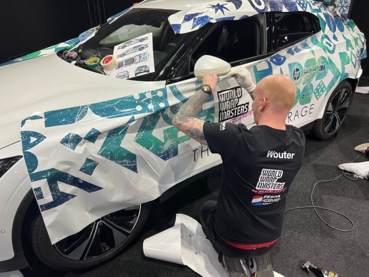 Wouter applies a blue and green patterned vinyl wrap to a car during the World Wrap Masters competition.