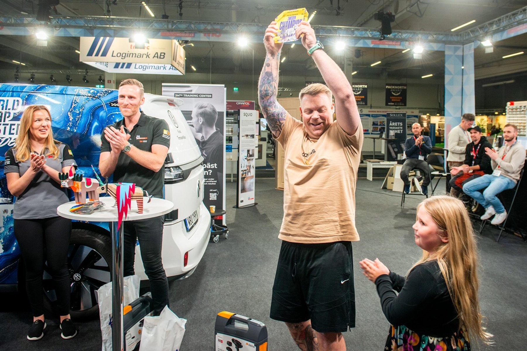 Winner holds up the 'Sweden Champion' prize, cheered by two adults and a young girl at the Wrap Masters event.